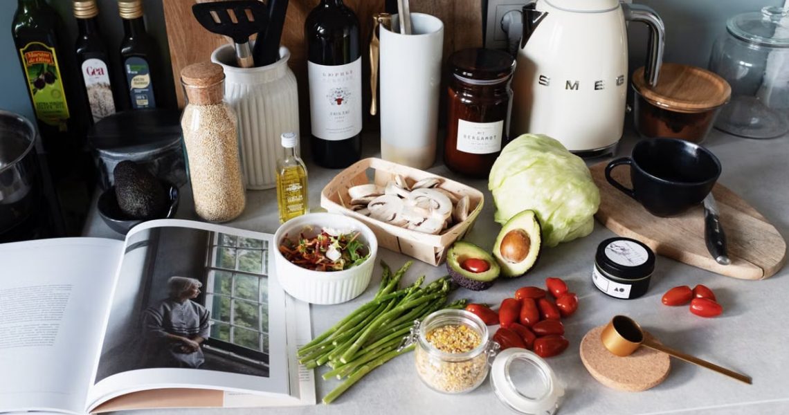 Various colorful healthy food and vegetables locating on countertop next to many different utensils and white kettle during cooking in stylish kitchen